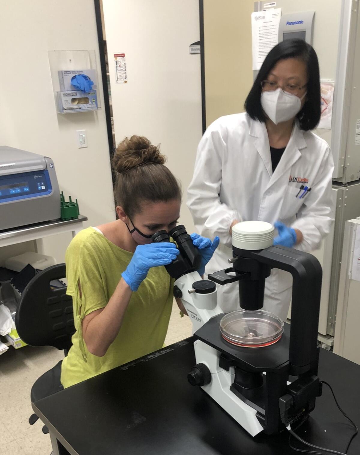 Michaelle Jinnette peers through a microscope while Dr. Qiong (June) Cao observes.