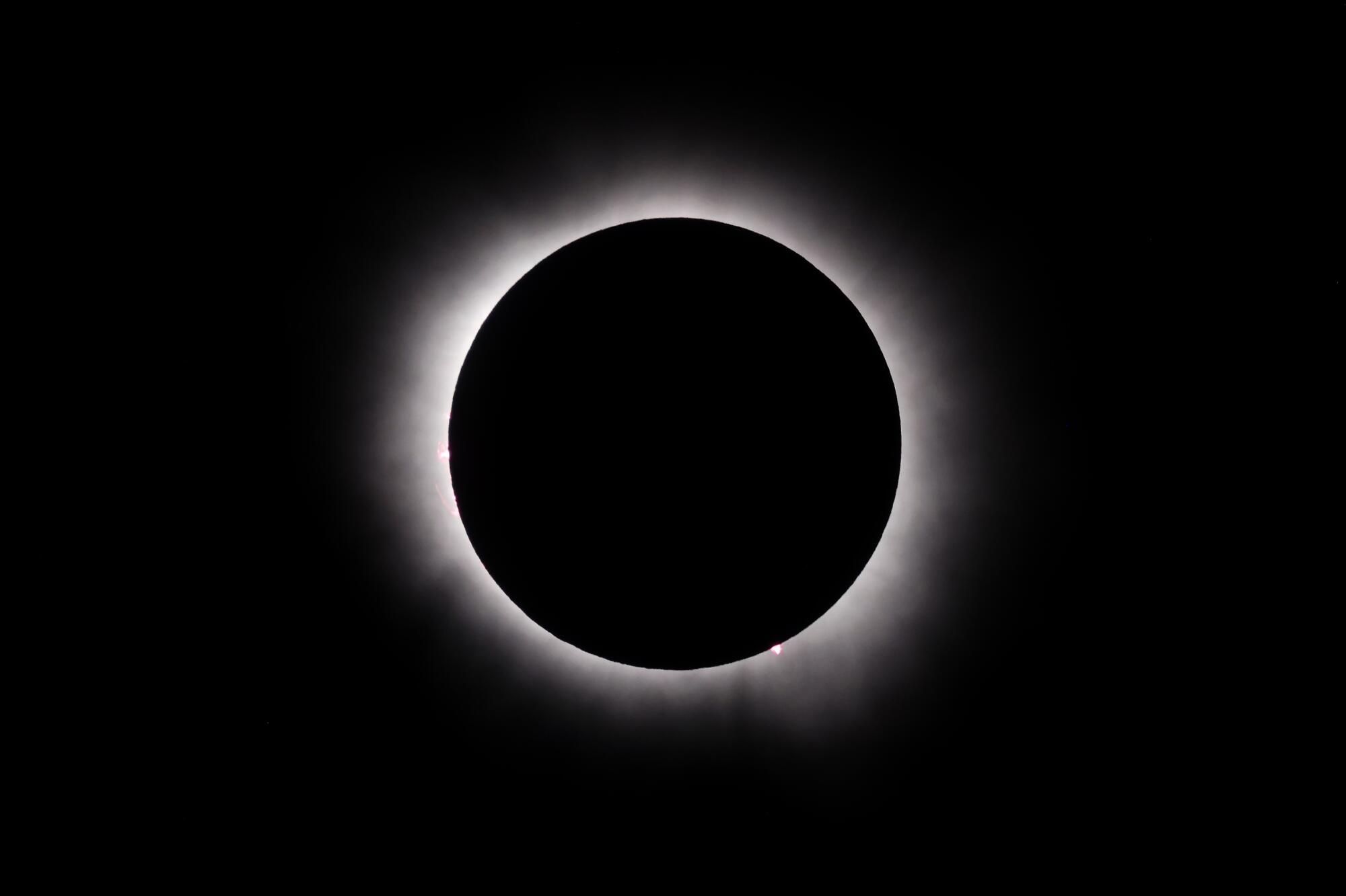 A black circle has white edges against a black background as the moon covers the sun during a total solar eclipse.