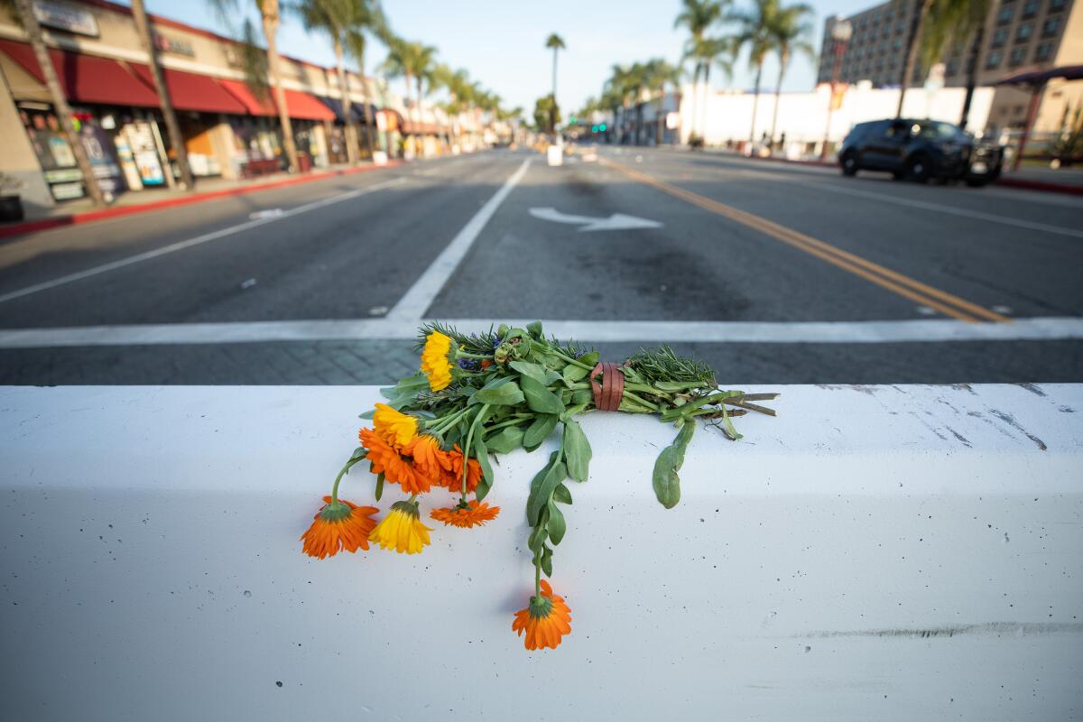 Orange flowers lie on a concrete barrier with an empty street behind.