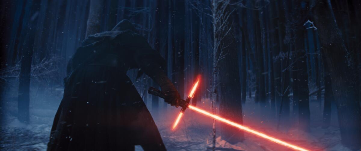 A black-cloaked movie character is seen from behind hunched forward in a dark forest and holding a T-shape red lightsaber