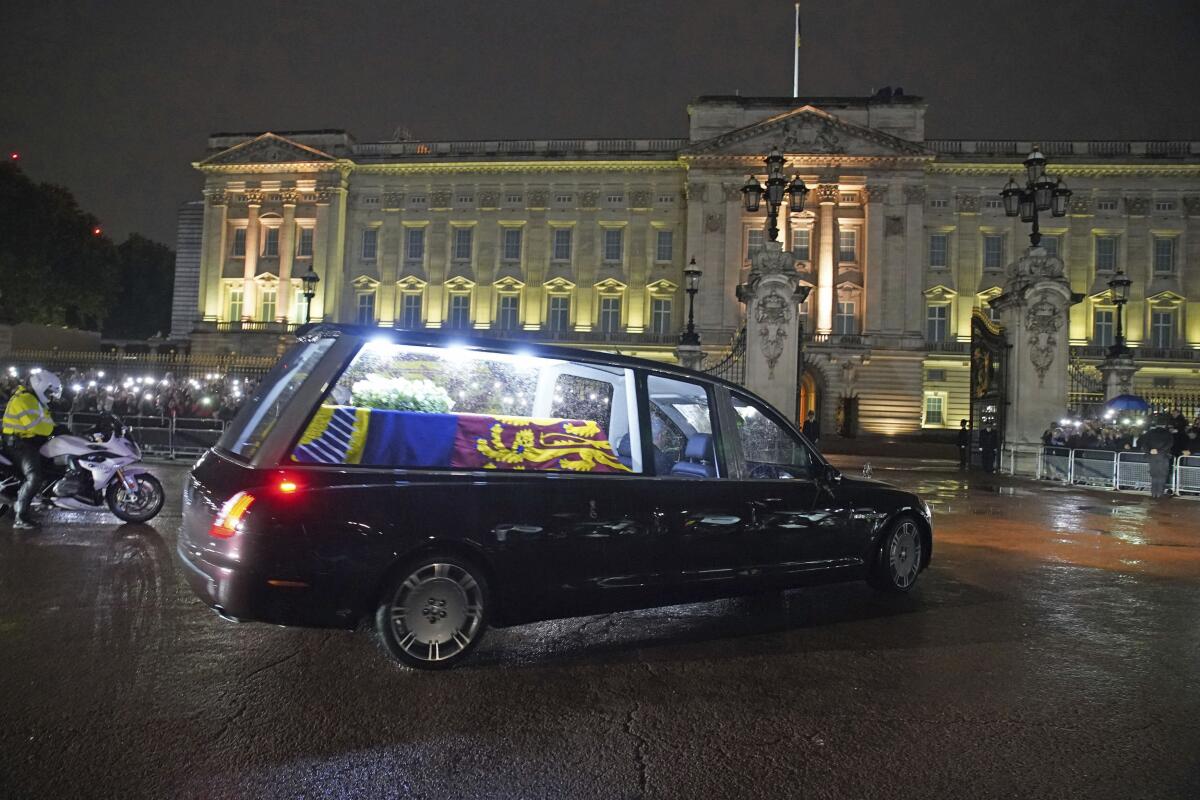 A hearse with a coffin approaches a grand building.