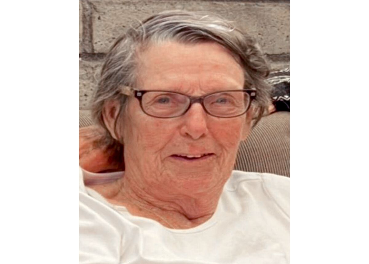 A head-and-shoulders portrait of an elderly white woman wearing glasses and smiling. 