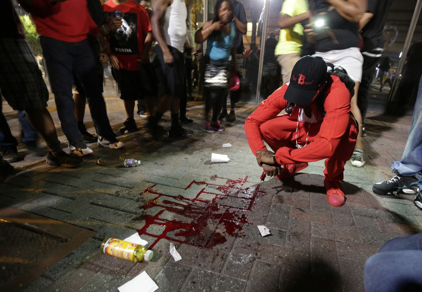 A protester sits near a pool of blood after a man was shot during a demonstration over the fatal police shooting of Keith Lamont Scott in Charlotte, N.C. The man, Justin Carr, later died at a local hospital, and police said they arrested and charged a man with with the shooting.