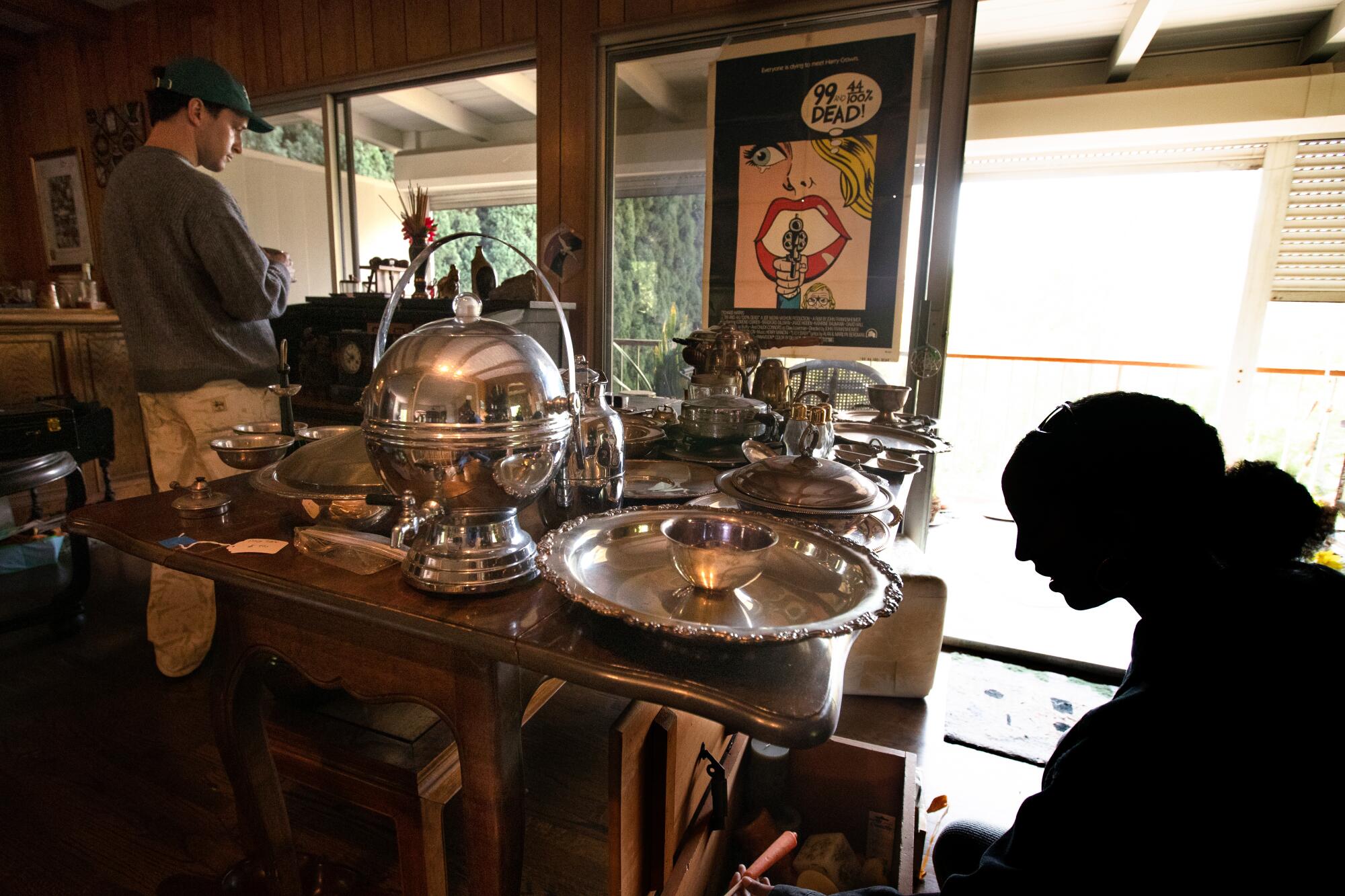 A woman looks at silver and other items on and under a table.
