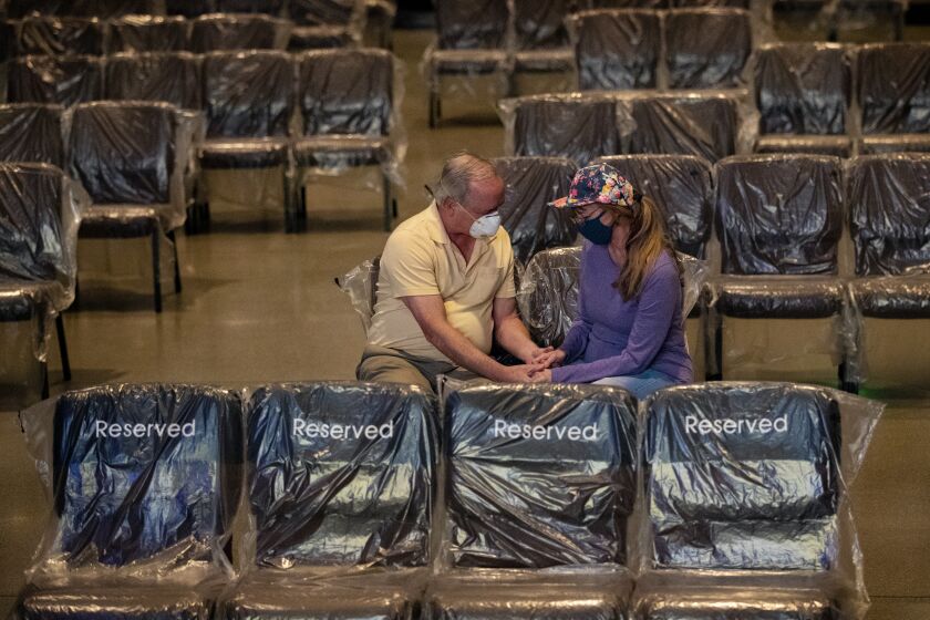 FONTANA, CA - MAY 30, 2020: Donald and Angie Autrey of Rancho Cucamonga pray before services begin at the reopening of the Water of Life Community Church during the coronavirus pandemic on May 30, 2020 in Fontana, California. The chairs have been covered in plastic and spaced out for social distancing. The stadium seating will not be used only the floor seating at 20% capacity. The plastic will be thrown out and new plastic used for each service.(Gina Ferazzi / Los Angeles Times)
