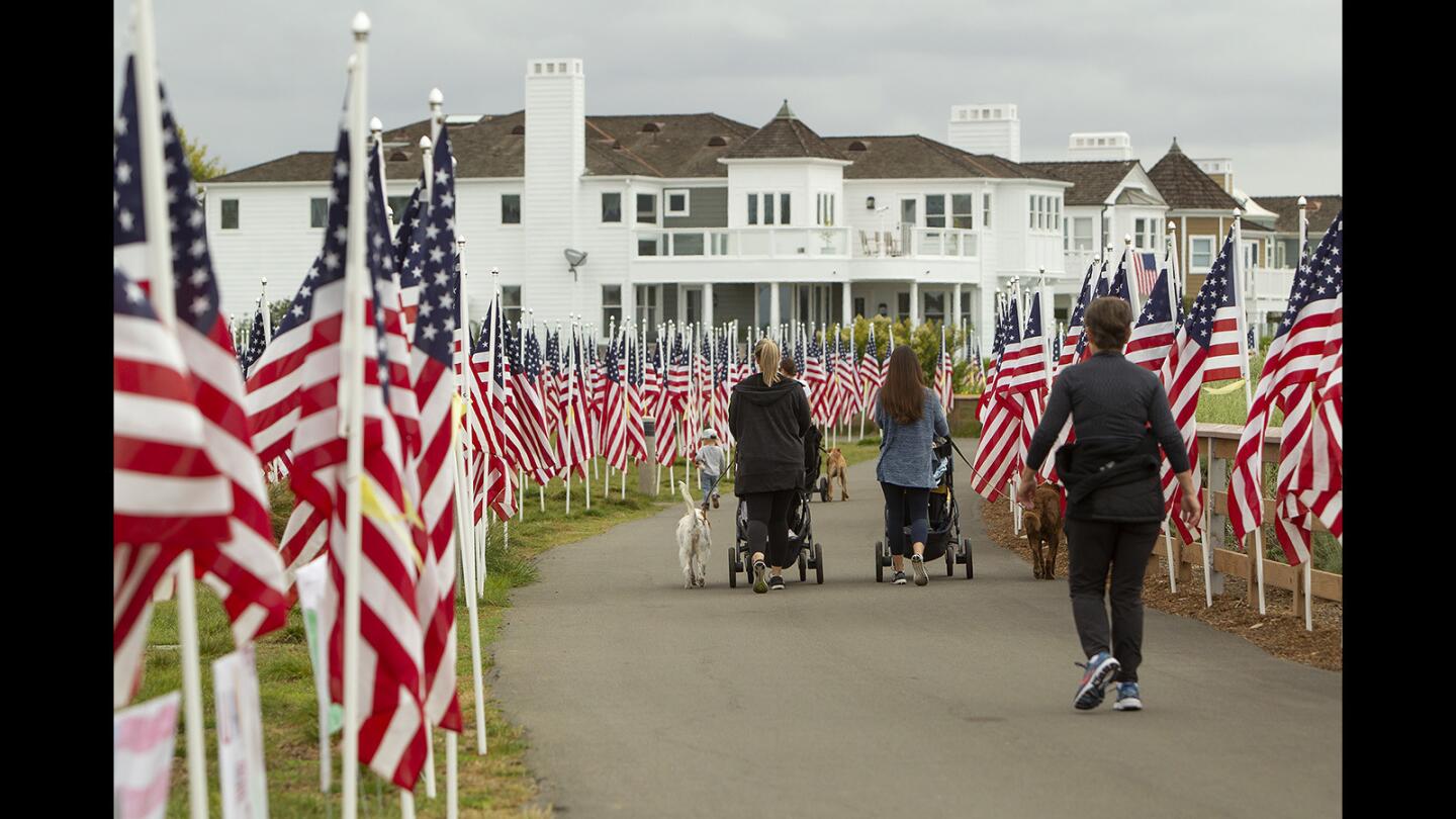 Morning walkers stroll through the Field of Honor, a display of 1,776 flags in remembrance of fallen military service members, at Castaways Park in Newport Beach on Tuesday. The Exchange Club of Newport Harbor is presenting the ninth annual exhibit through Monday, Memorial Day.