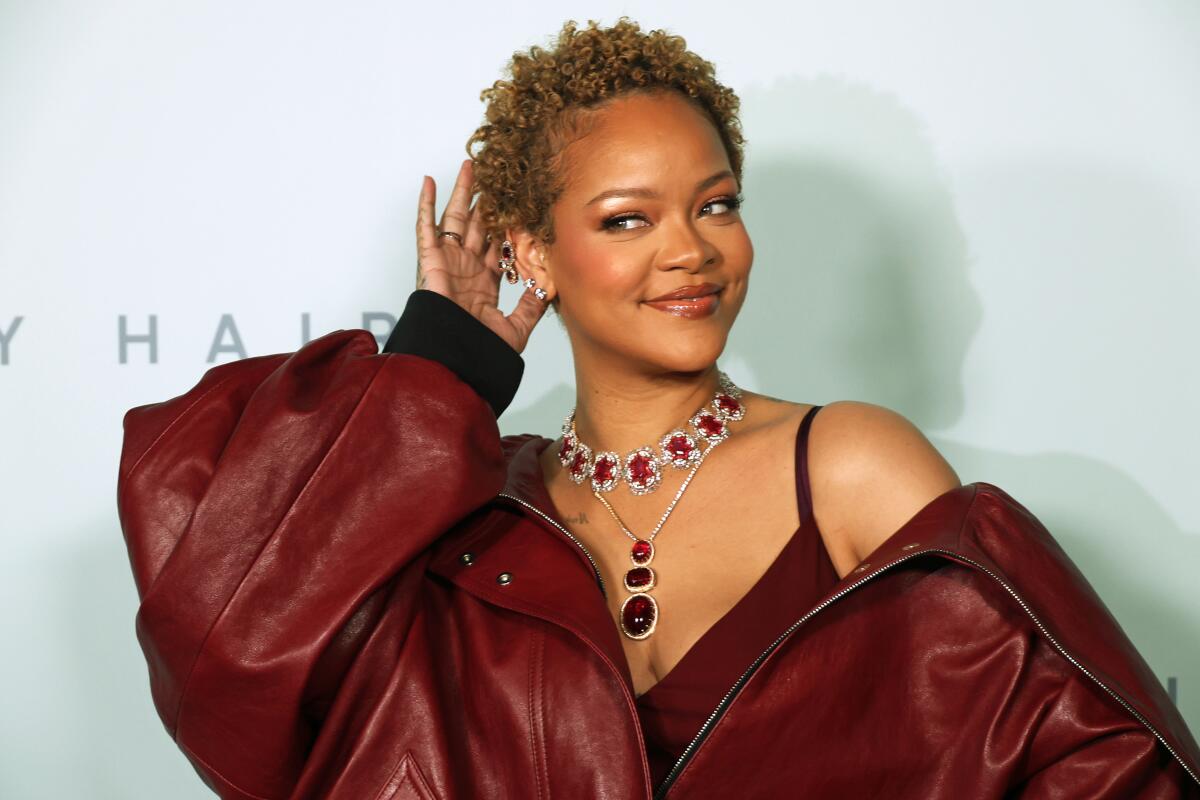 Rihanna shows off her short curls while wearing a maroon dress, matching leather jacket and sparkling jewelry
