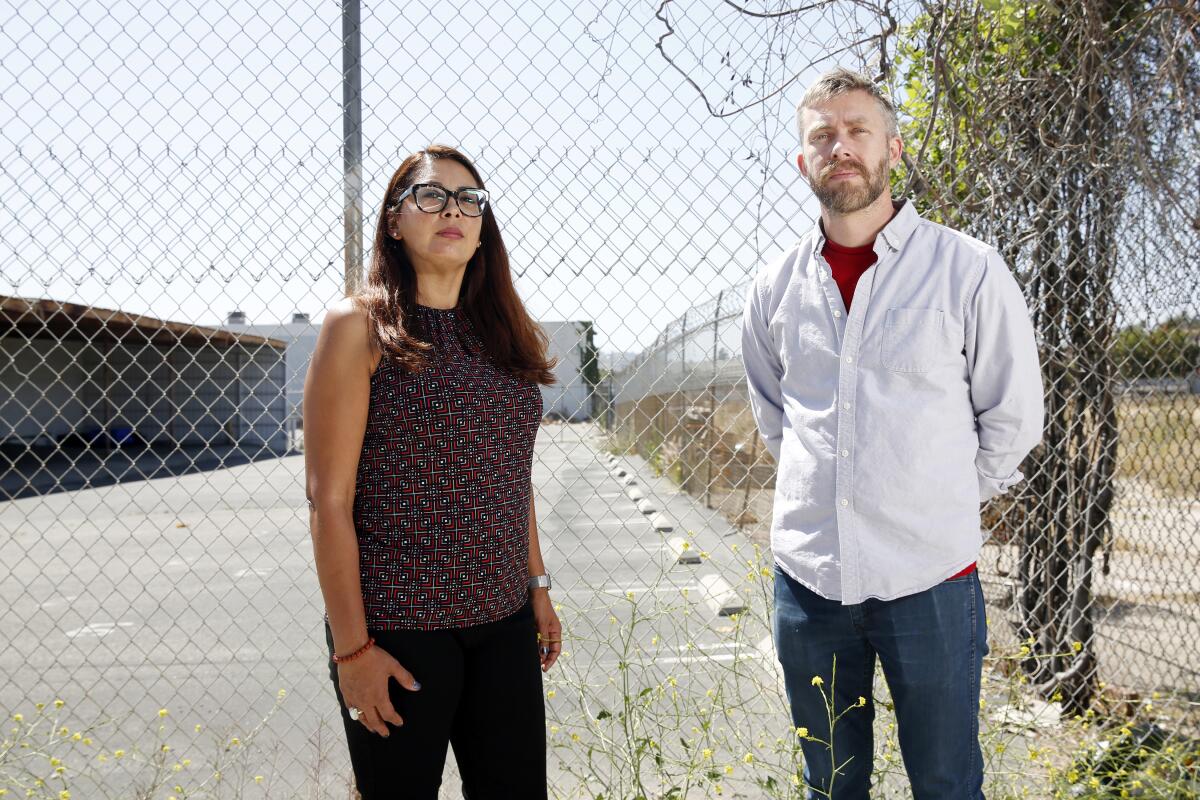 Two people stand in front of a chain-link fence.