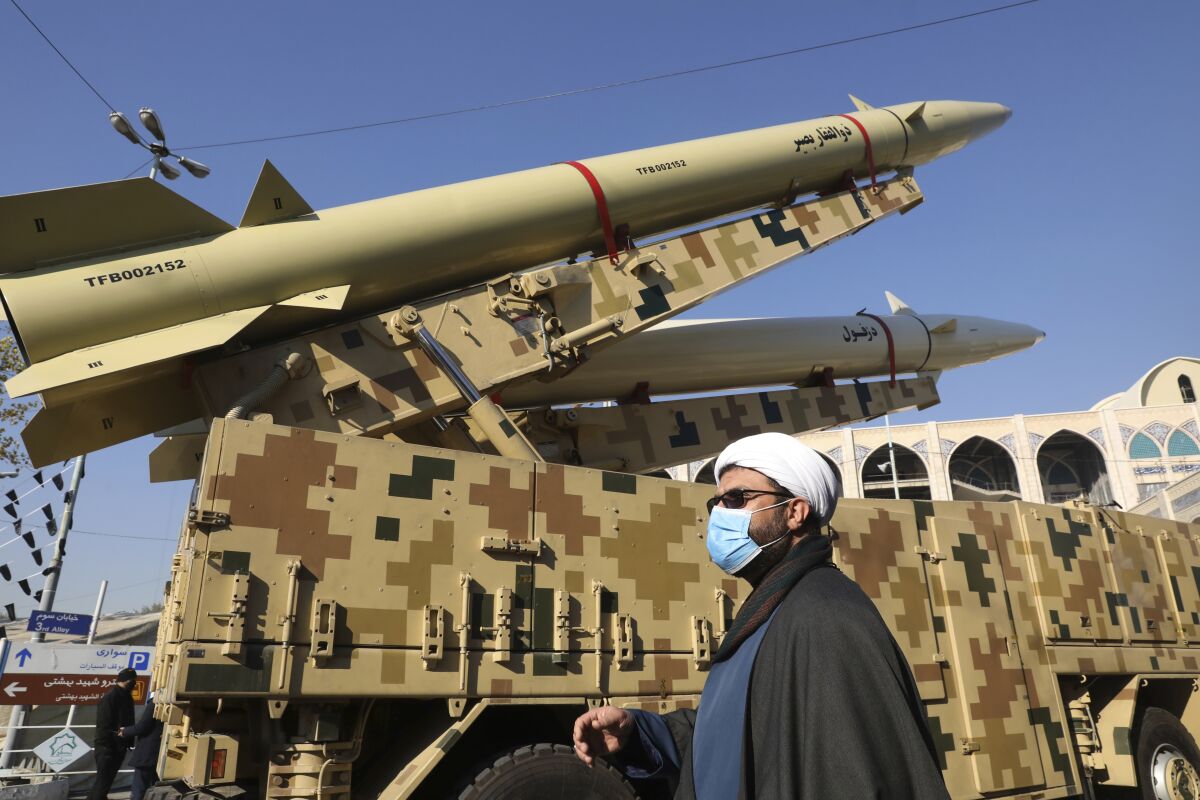 ADDS NAME OF MISSILES - A cleric walks past Zolfaghar, top, and Dezful missiles displayed in a missile capabilities exhibition by the paramilitary Revolutionary Guard a day prior to second anniversary of Iran's missile strike on U.S. bases in Iraq in retaliation for the U.S. drone strike that killed top Iranian general Qassem Soleimani in Baghdad, at Imam Khomeini grand mosque, in Tehran, Iran, Friday, Jan. 7, 2022. Iran put three ballistic missiles on display on Friday, as talks in Vienna aimed at reviving Tehran's nuclear deal with world powers flounder. (AP Photo/Vahid Salemi)