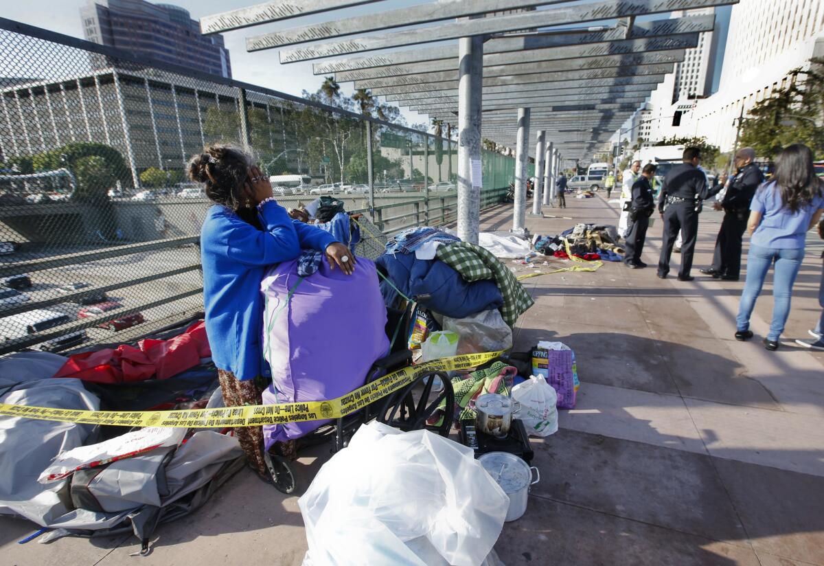 Ry Thounry packs up her tent on the Main Street overpass above the 101 Freeway in downtown Los Angeles near police officers.