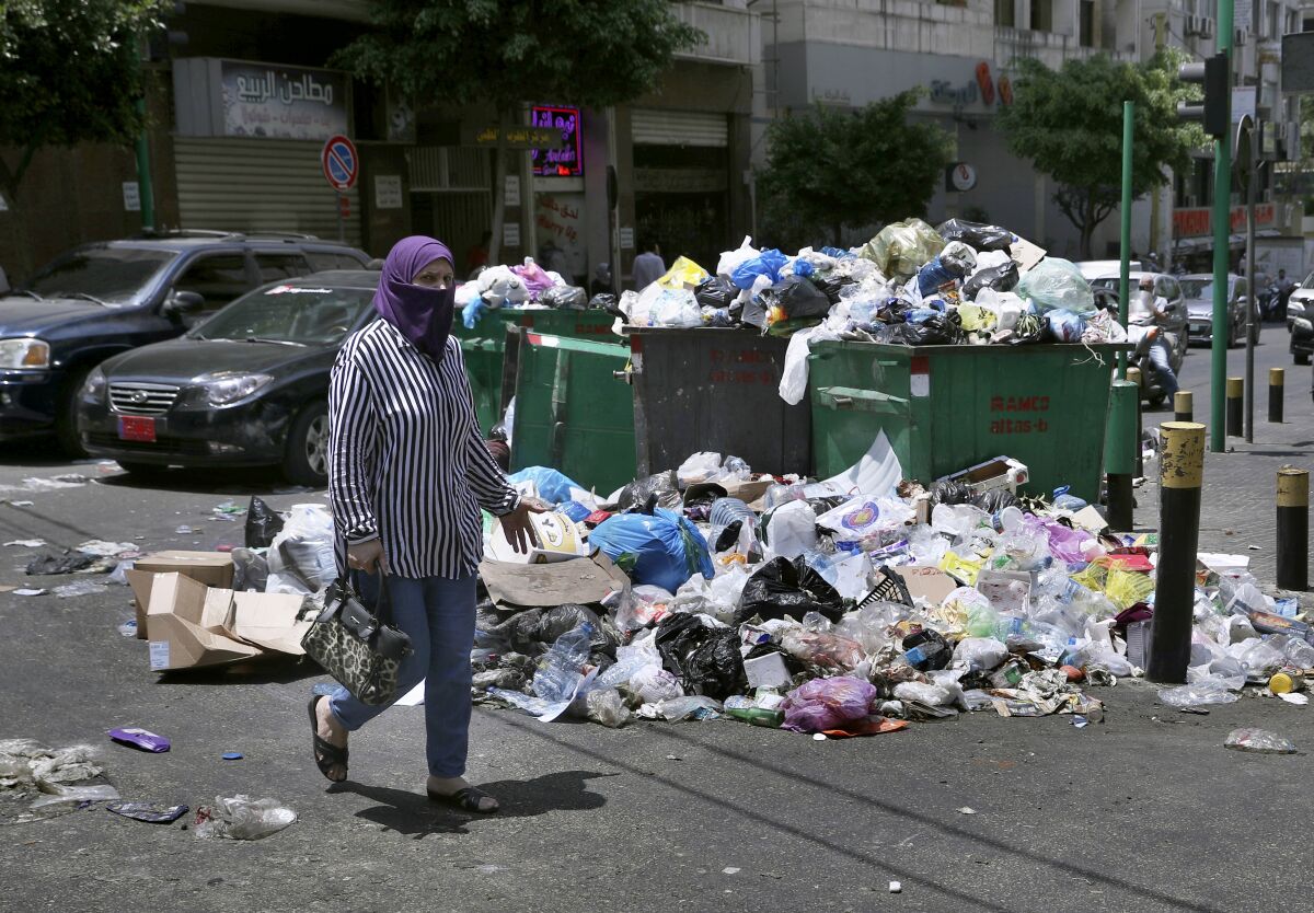 Beyrut caddesinde çöp yığınının yanından geçen kadın