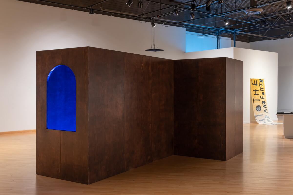 Emerald blue light emanates from a geometric, architectonic structure in the middle of a museum gallery