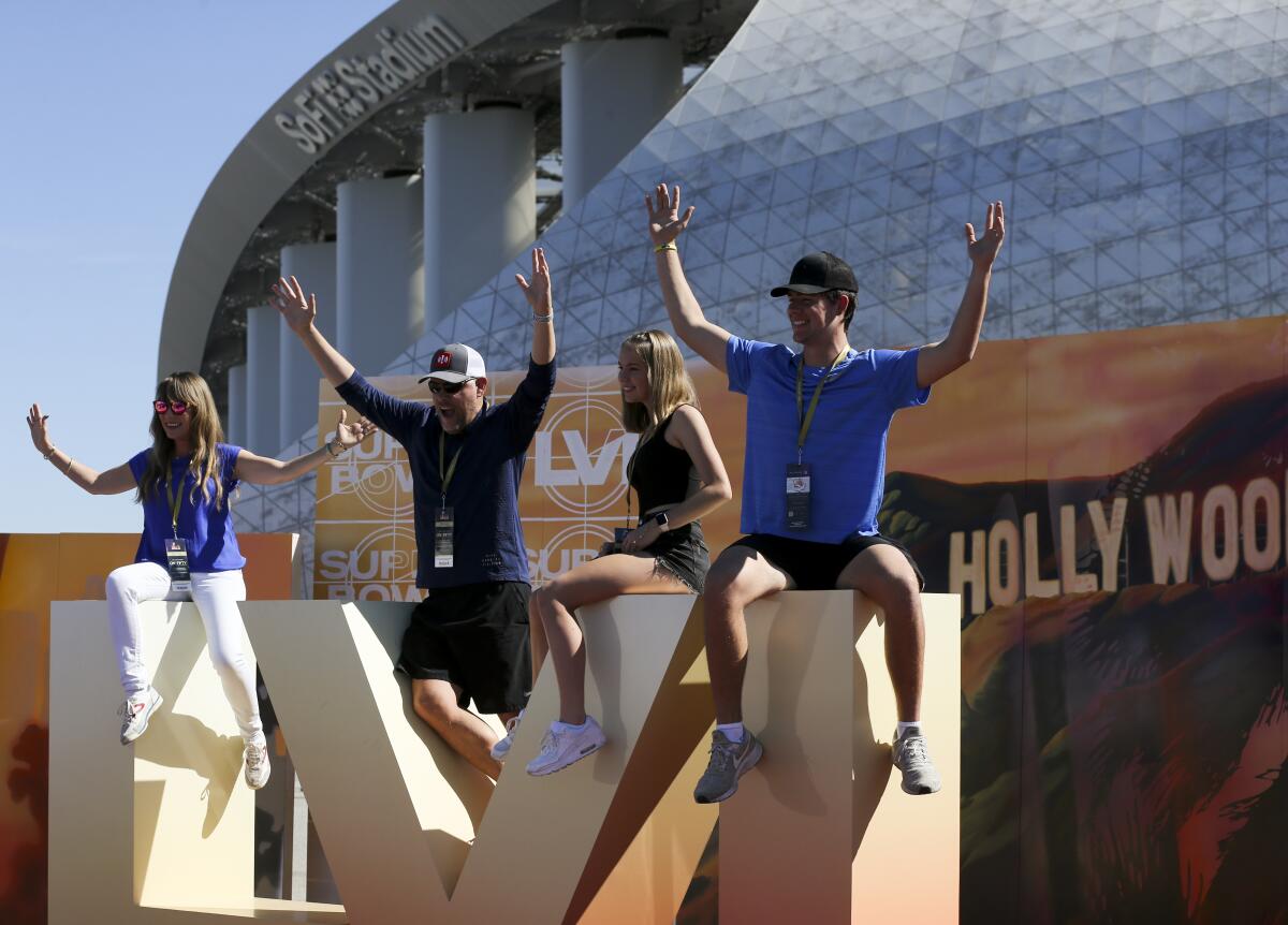 Fans sit on a sign for Super Bowl LVI outside of SoFi Stadium