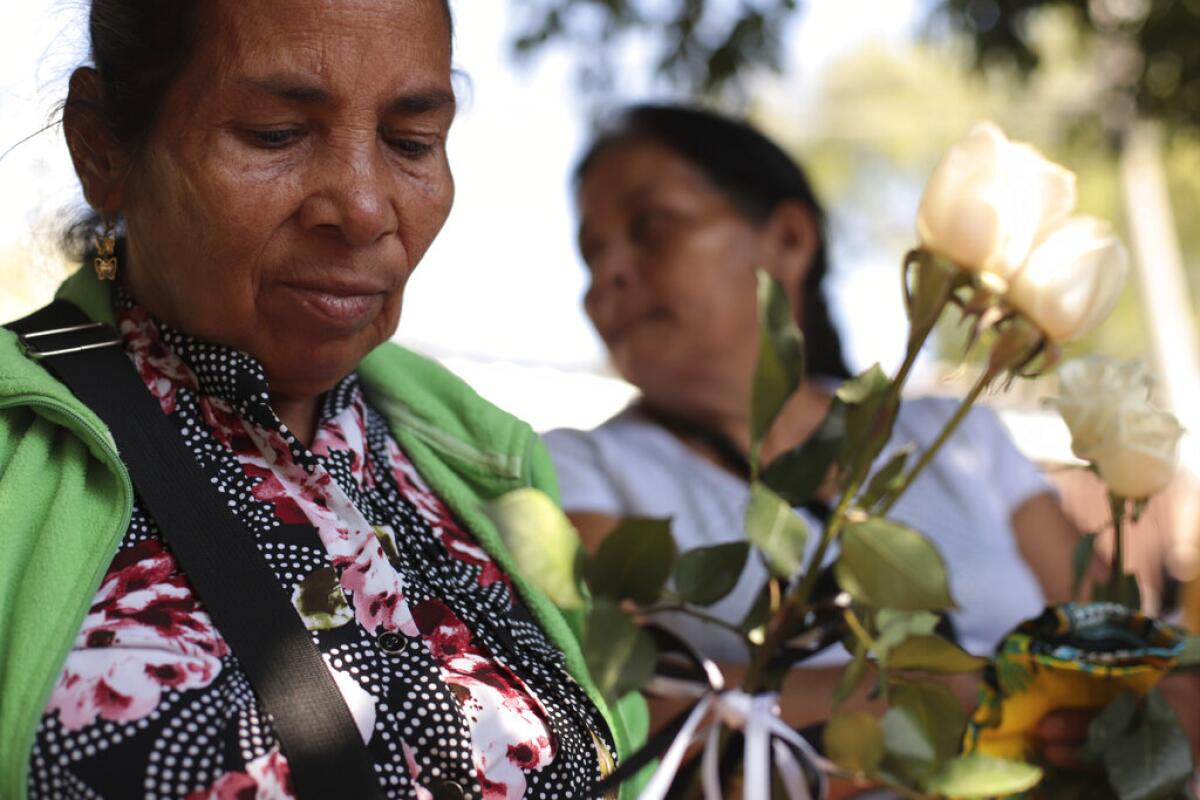 Juana de Jesús Regaleño Bonilla, de 66 años, sostiene rosas blancas mientras espera con sus familiares para recibir seis pequeños ataúdes que contienen restos de los familiares que perdió en una masacre de 1982, en San Salvador, El Salvador, el jueves 23 de enero de 2020. (AP Foto/Salvador Melendez)