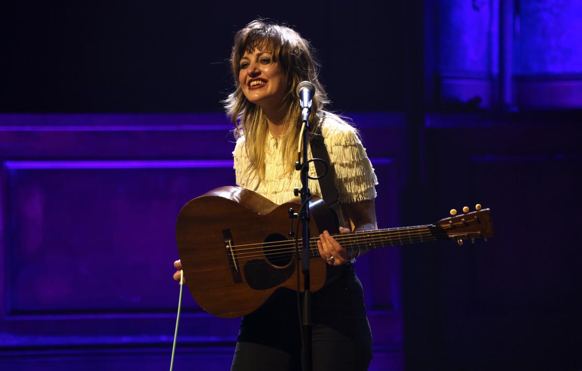 Anaïs Mitchell onstage smiling and holding a guitar.