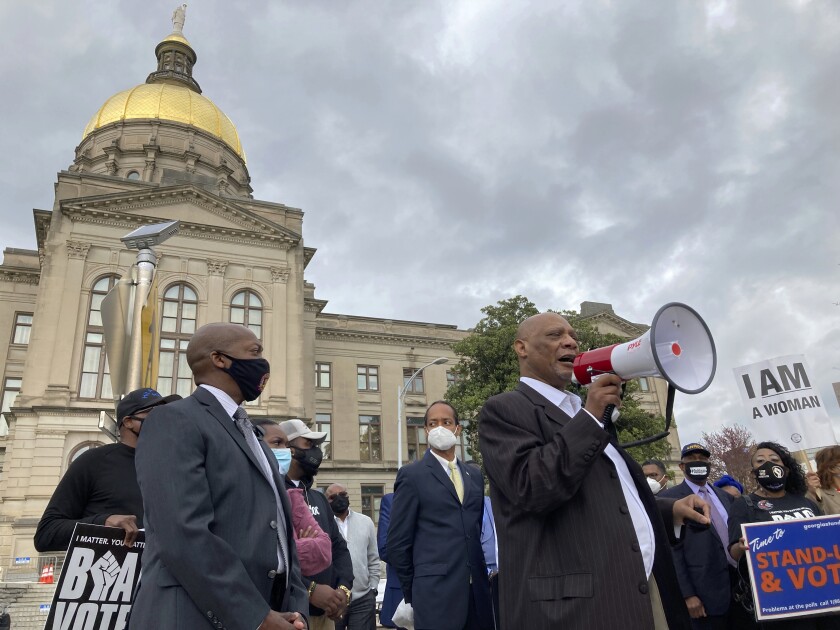 A man speaks into a megaphone in front of the Georgia state Capitol building with a group of people holding protest signs