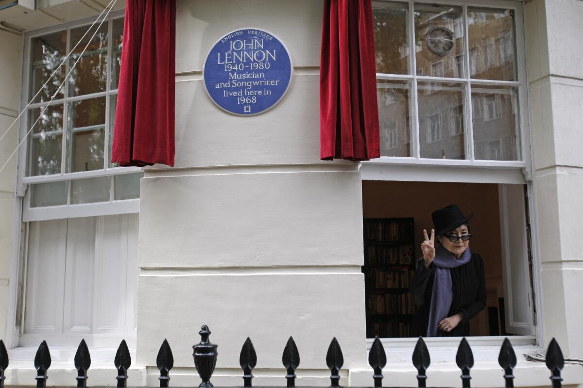 Yoko Ono in window of building with a plaque honoring John Lennon