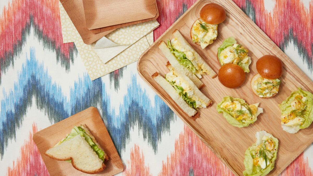 Jammy Egg Salad on sandwiches with tomatoes displayed on wooden boards atop patterned fabric.