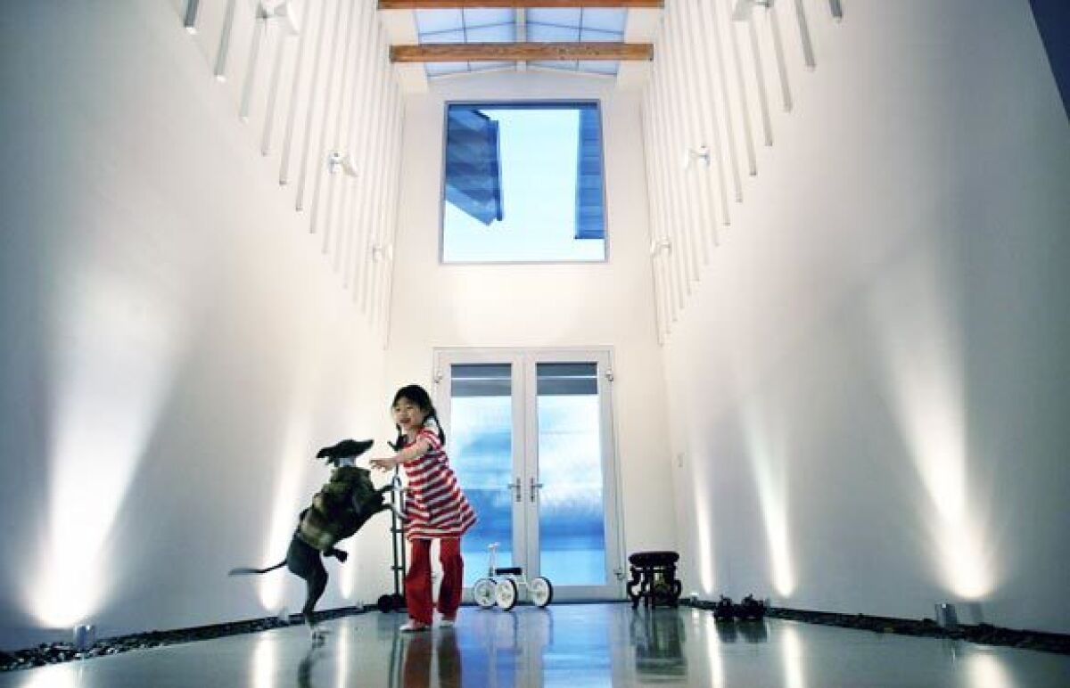 When Vanessa Choy and Andrew Wong closed their architecture practice in Hong Kong and moved to Los Angeles, they bought a Studio City lot and made plans for a farmhouse with a distinctly modern vibe. Here, daughter Jillian, 5, plays with the family dog in the entry hall, where the vertical lines of the house's board-and-batten exterior are repeated in the transition from the outside to the inside. Spotlights and troughs of pebbles line the walls; above lies a fiberglass sunroof.