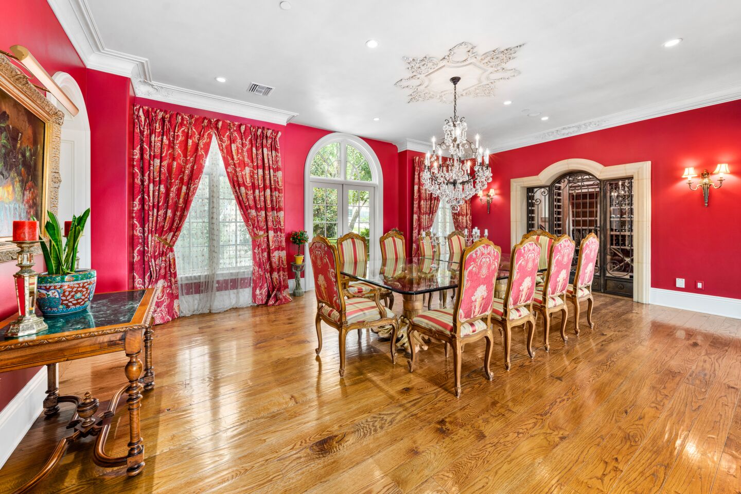 The dining room is red with curtains in front of windows and a formal dining set.