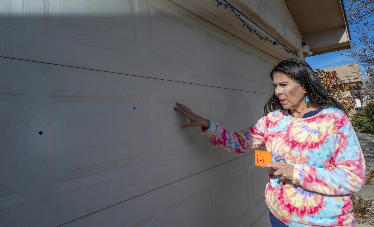 A woman indicates bullet holes in a garage door