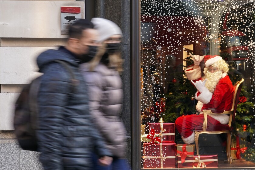 A man dressed as Santa Claus gestures as people walk past, in London, Saturday, Dec. 4, 2021. Britain says it will offer all adults a booster dose of vaccine within two months to bolster the nation's immunity as the new omicron variant of the coronavirus spreads. New measures to combat variant came into force in England on Tuesday, with face coverings again compulsory in shops and on public transport. (AP Photo/Alberto Pezzali)