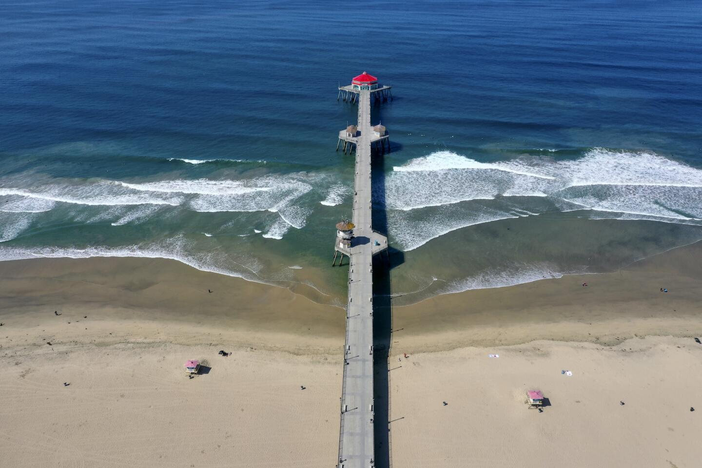 An aerial view of a mostly empty beach and surfers defying Gov. Newsom's "hard close" of Orange County beaches.