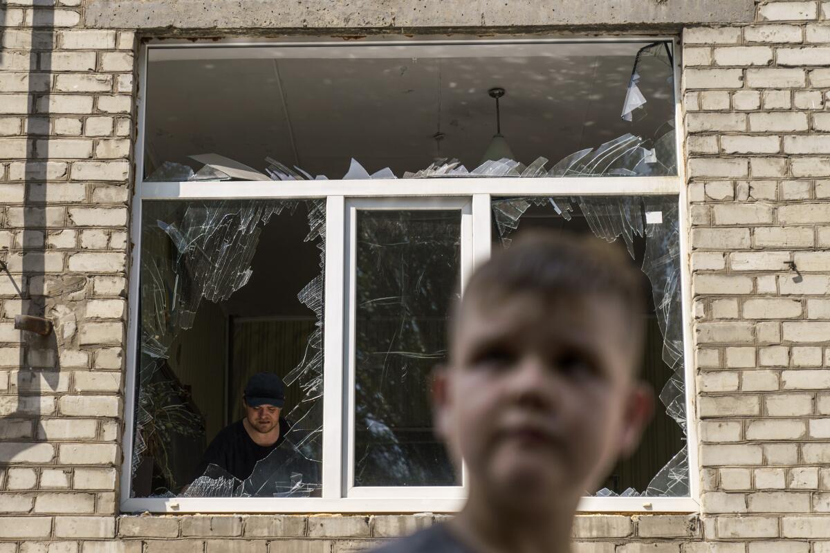 A man is seen through broken windows in a brick building, a boy's face in the foreground
