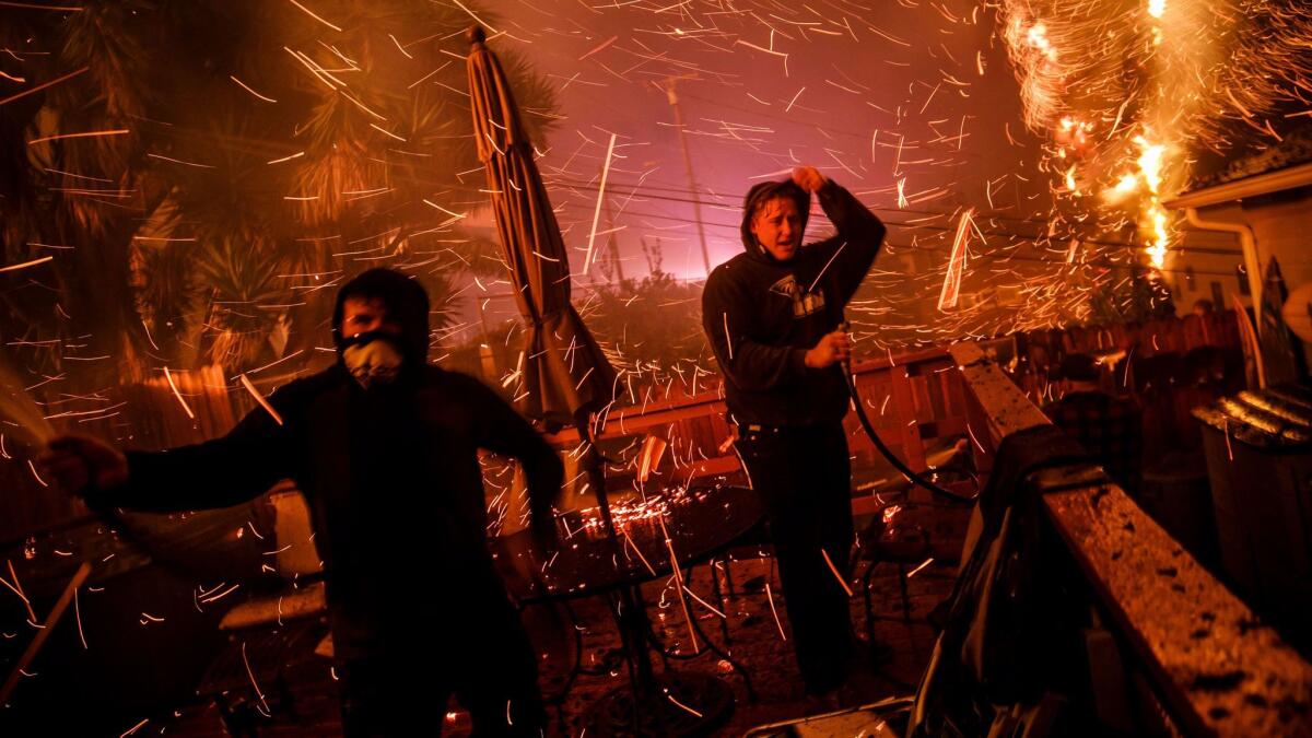 John Bain, left, and Brandon Baker take cover from embers as they try to help stop a fire from burning a stranger's home in Ventura.