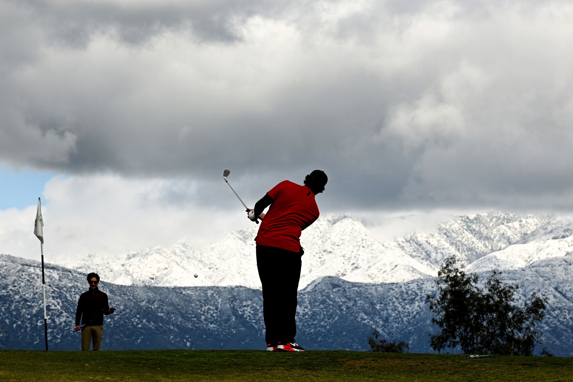 A golfer mid-swing on a cloudy day with snowy mountains in the background