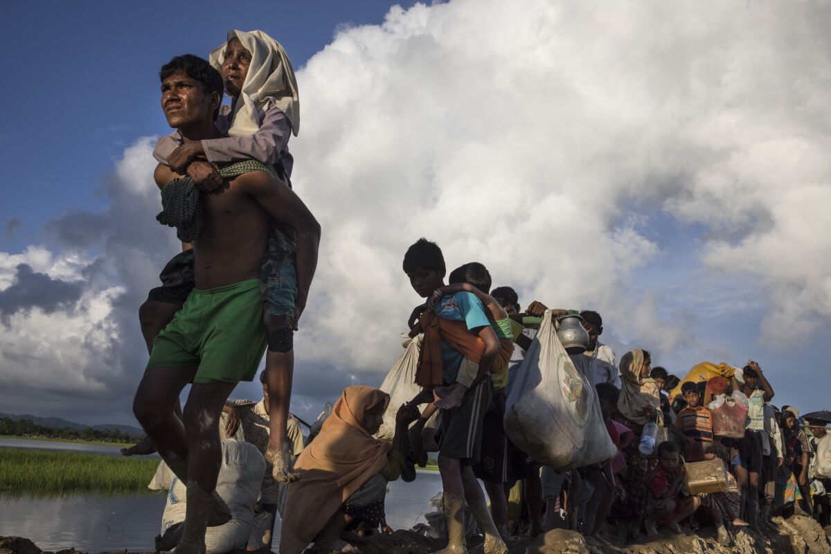 A man carrying a woman on his back leads a line of refugees.
