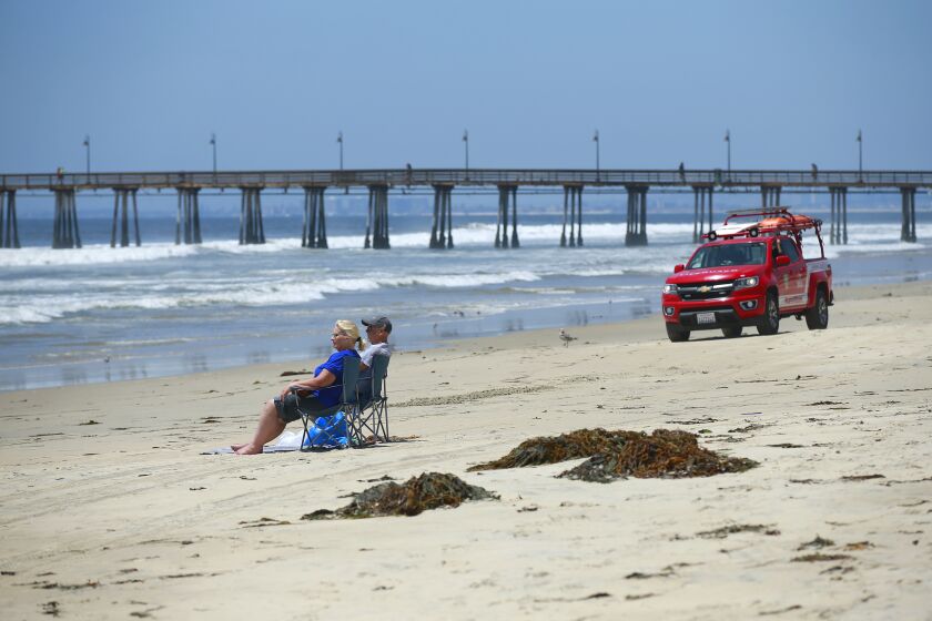 Tourists sit on a nearly empty stretch of beach as lifeguards drive by in Imperial Beach on May 30, 2019. Recent rains have contaminated the ocean water and closed many of the beaches (including Imperial Beach) in the region near the mouth of the Tijuana River.