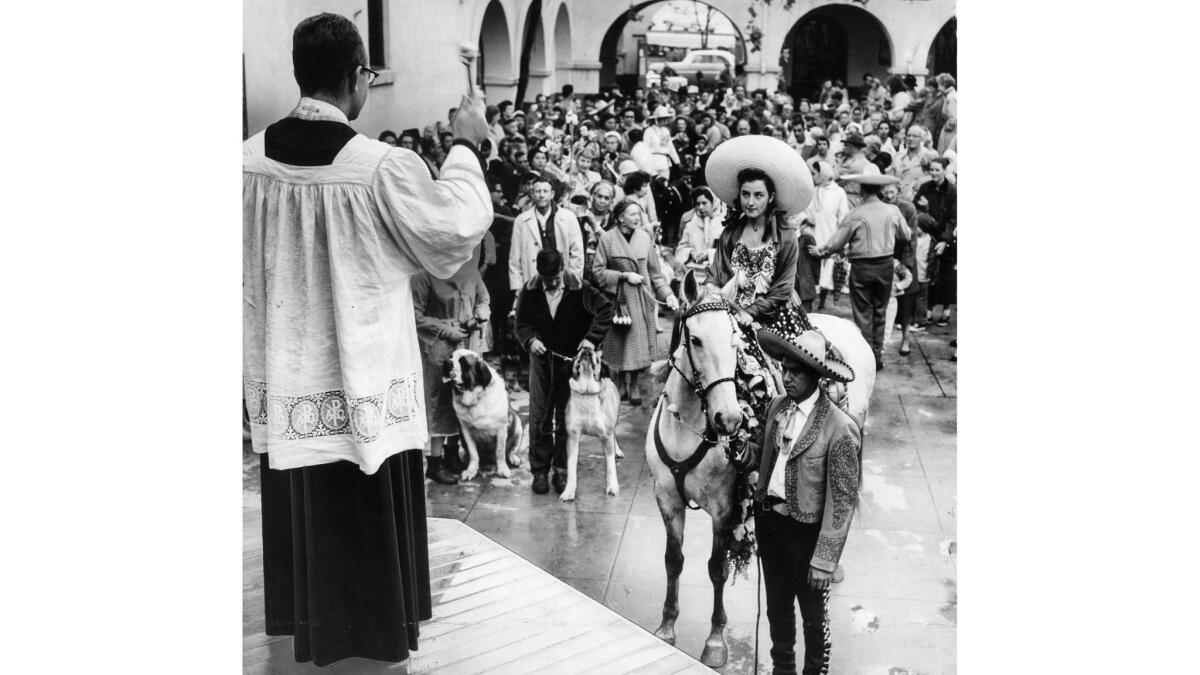 April 20, 1957: The Rev. Raymond Reha blesses animals in the courtyard of the Old Plaza Church. First in line was Marta Robles on horse. Others await their turn.