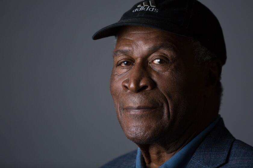 John Amos poses in a blue adidas hat and a blue collared shirt.