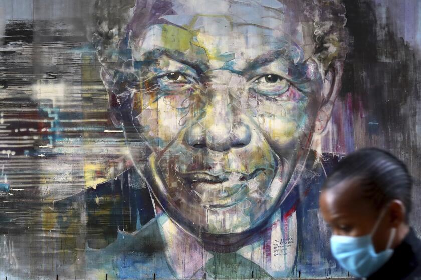 A woman wearing a face mask walks past a mural of former President Nelson Mandela in Cape Town, South Africa, Saturday July 18, 2020, as the country celebrates International Mandela Day. Mandela's fight for freedom and human rights makes him the most influential person among Africa's youth, according to a survey conducted across the continent. (AP Photo/Nardus Engelbrecht)