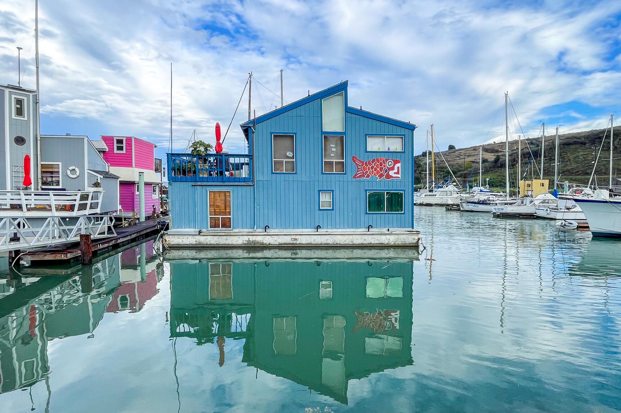 A blue building sits on the water in a marina among boats.