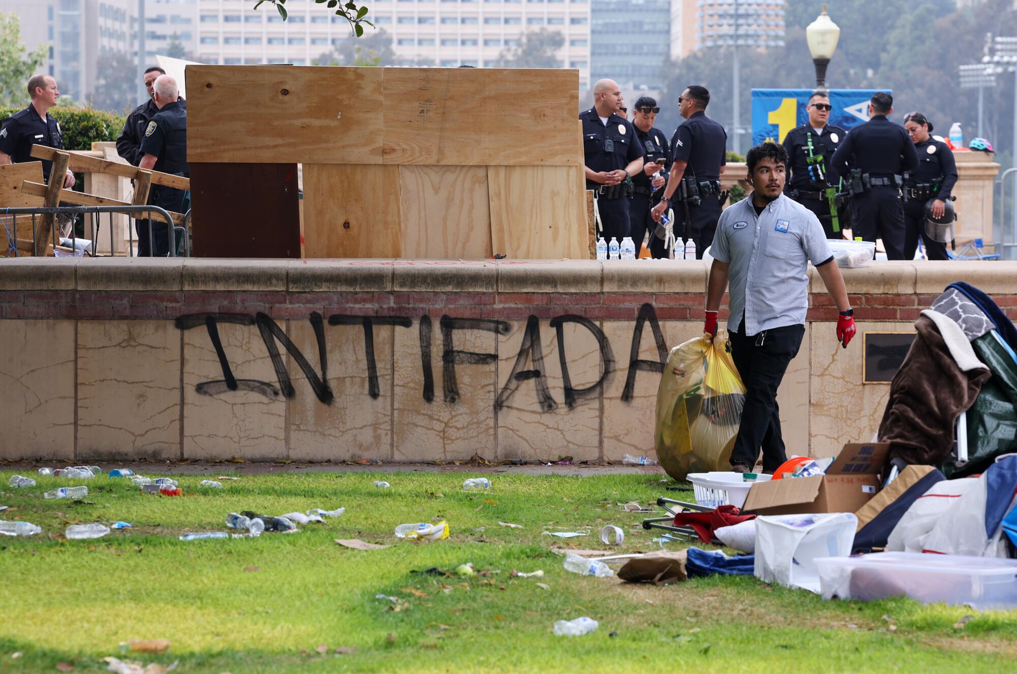 Um trabalhador da UCLA carregando uma sacola grande, com policiais ao fundo e a palavra "Intifada" rabiscado em uma barreira