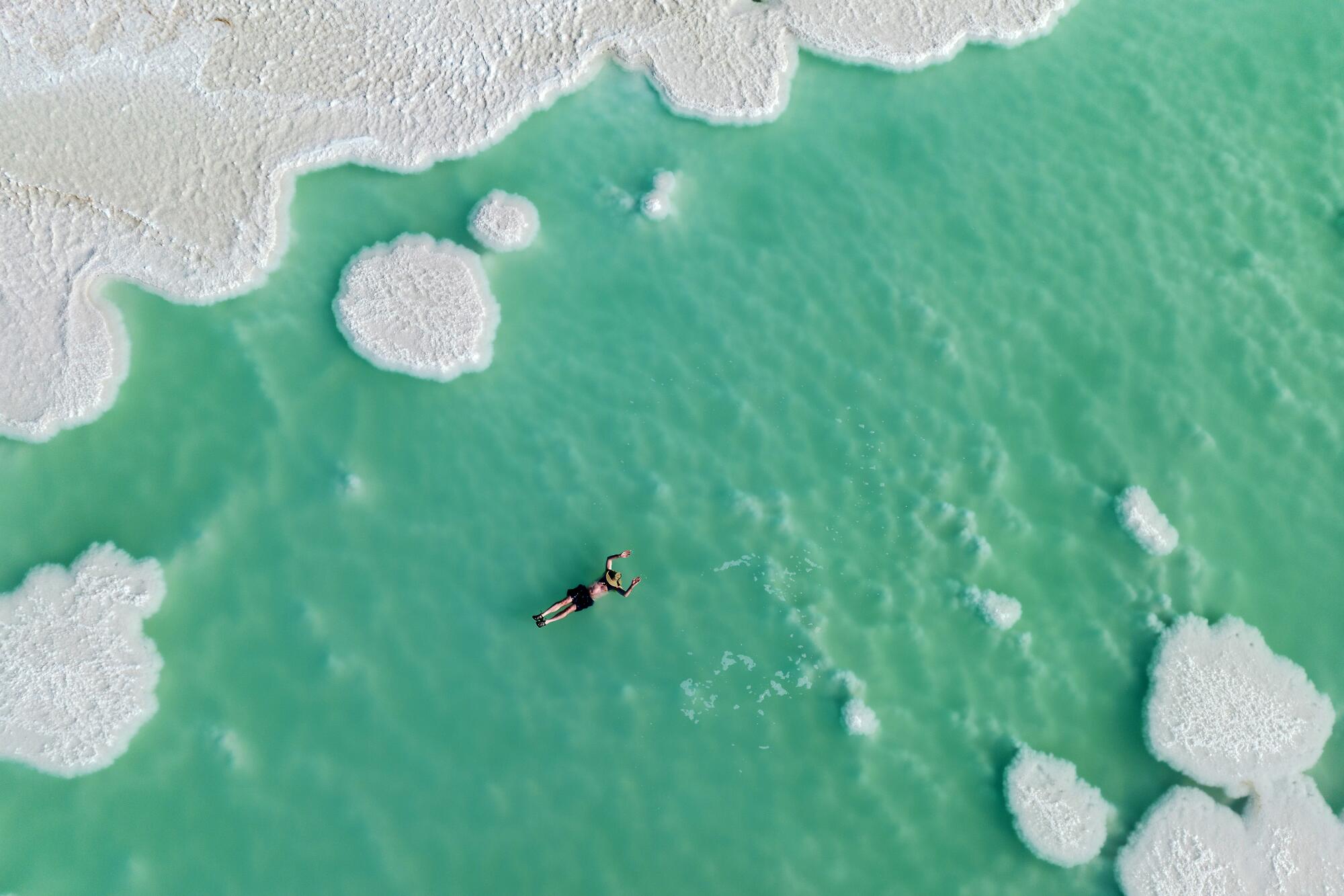 A drone photo showing a man floating in a vast, green-tinted body of water.