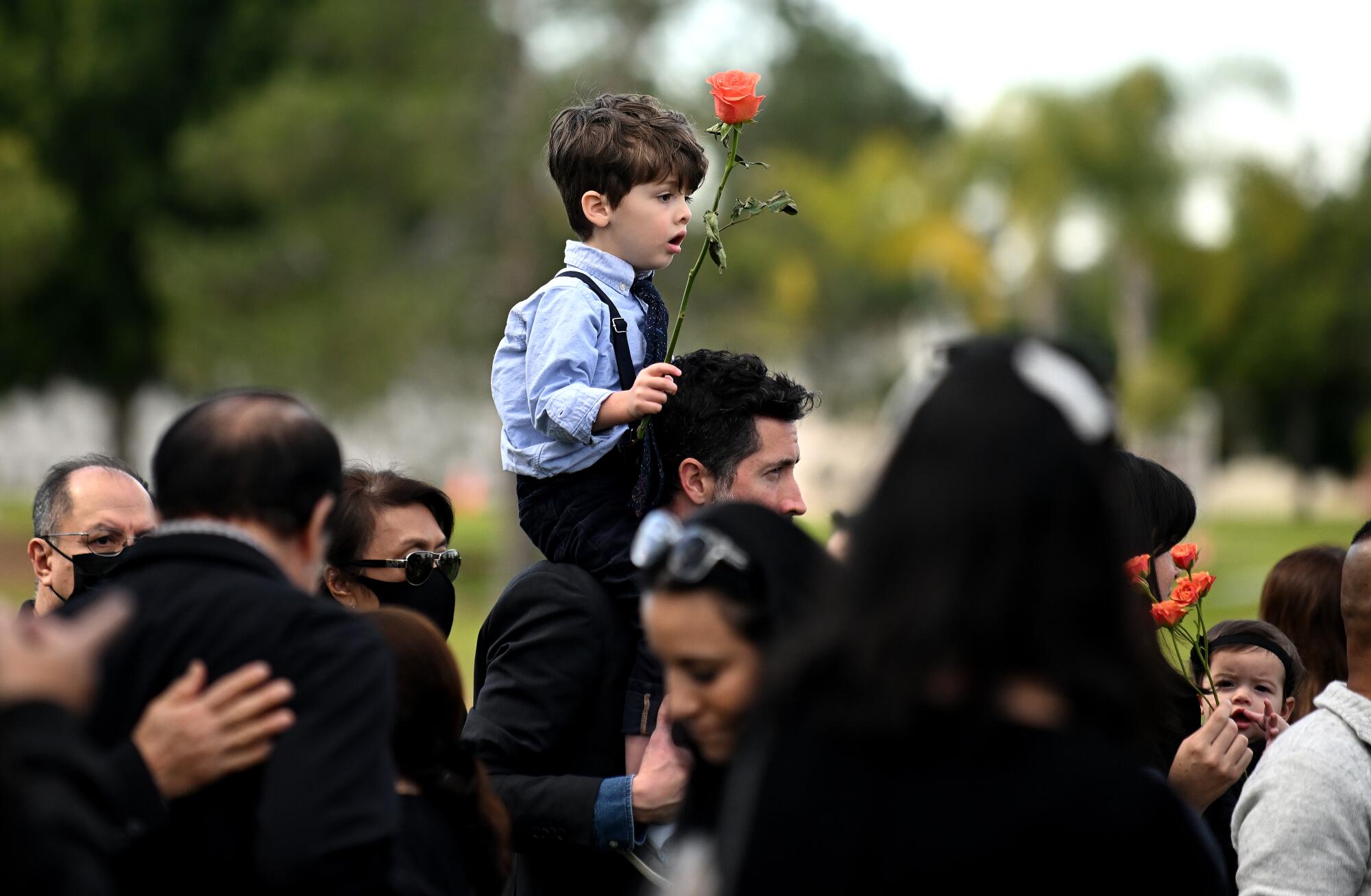 A boy holds a flower before placing it on the casket  at Resurrection Cemetery.