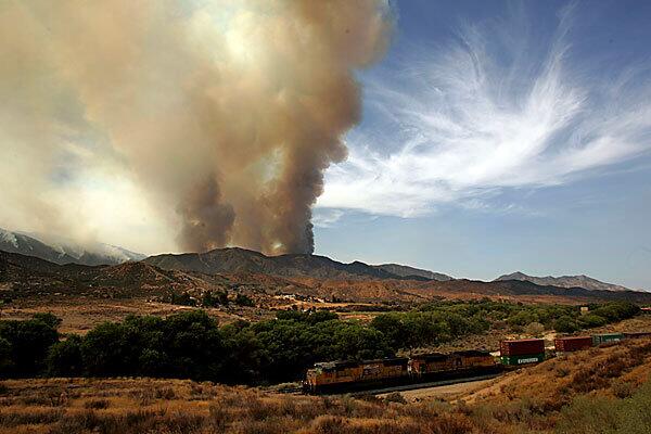 A cargo train passes through Acton as a plume of smoke rises from the Station fire.