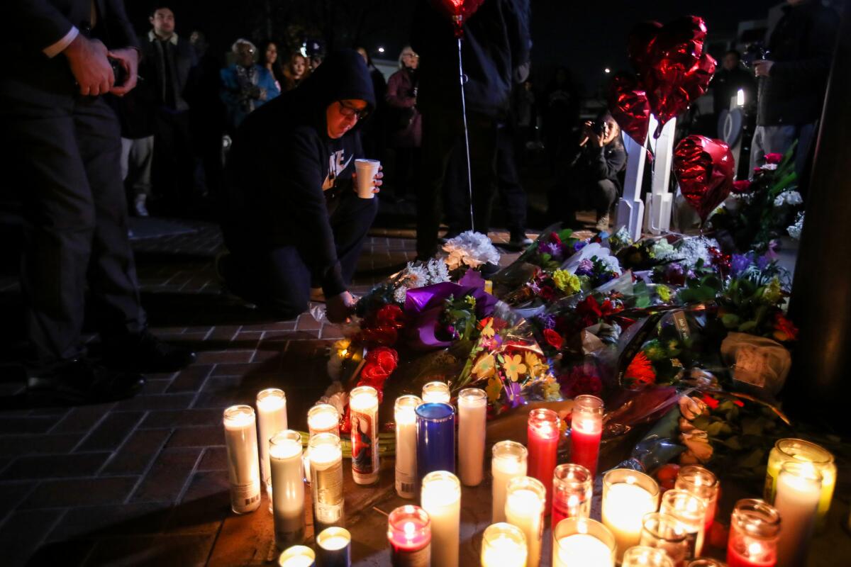 A person kneeling in front of   flowers and candles placed to honor shooting victims