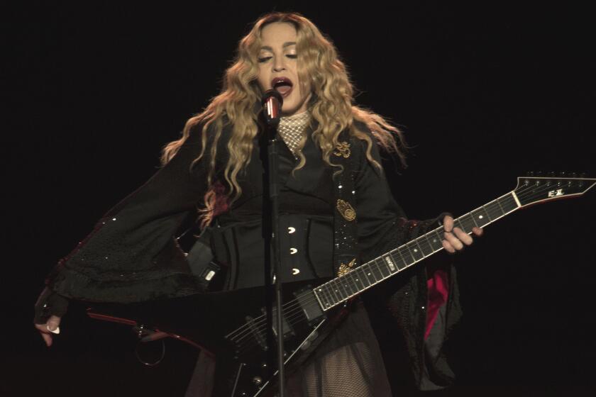 Madonna plays guitar while singing onstage wearing black