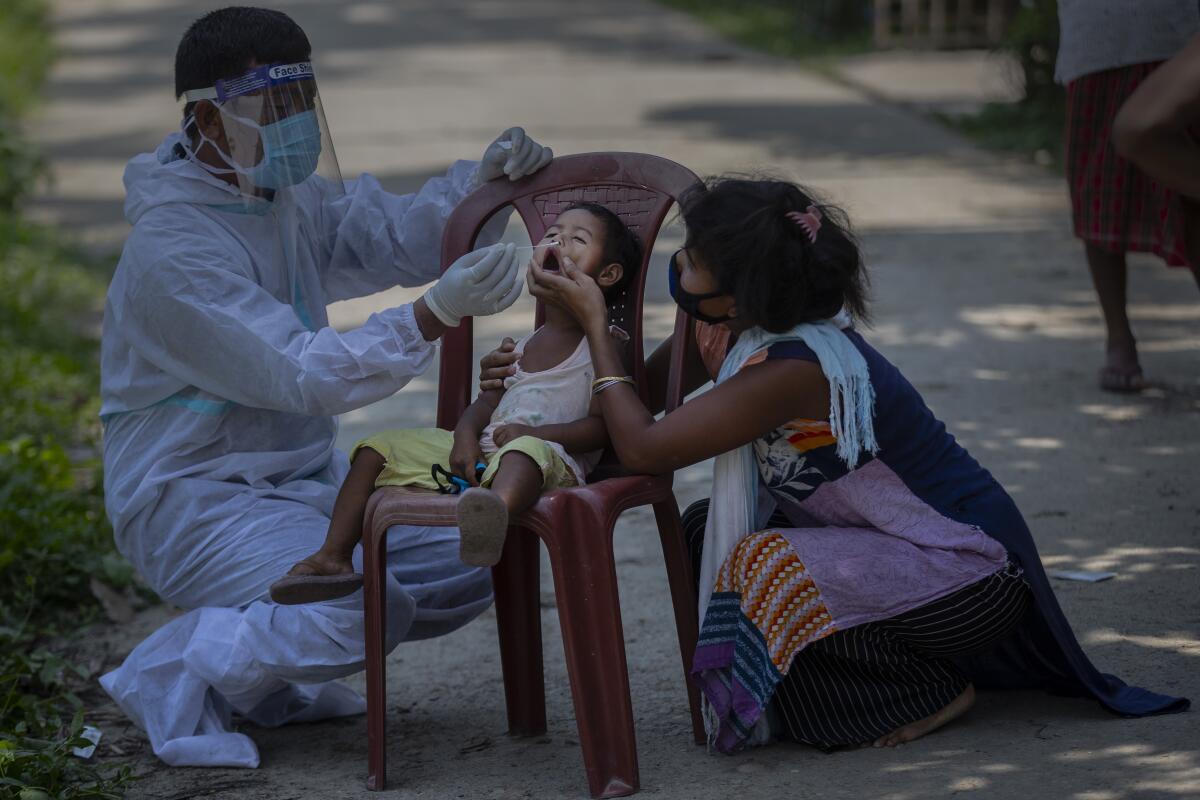 Child in chair being tested for coronavirus by health worker while woman holds child's chin