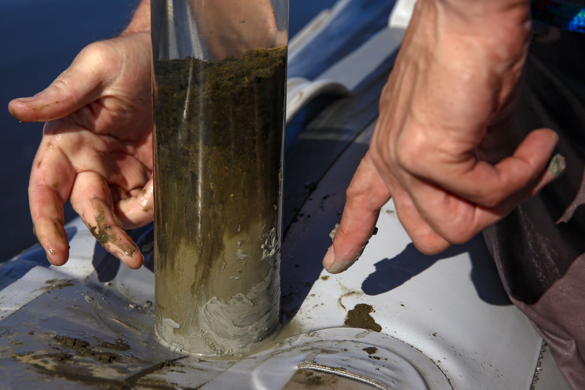 A person's hands point to a tube of mud and sediment.