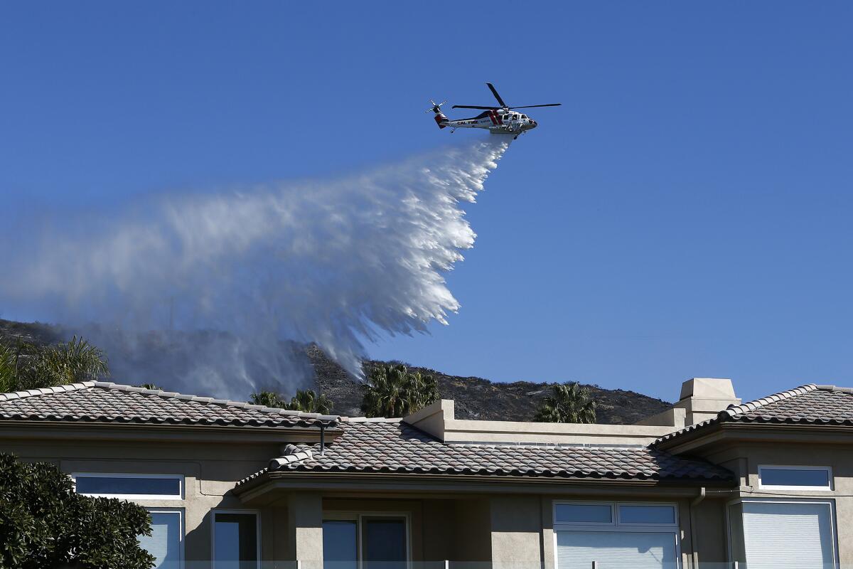 A Cal Fire helicopter dumps water over a burned hillside behind a home at Irvine Cove in Laguna Beach on Thursday.