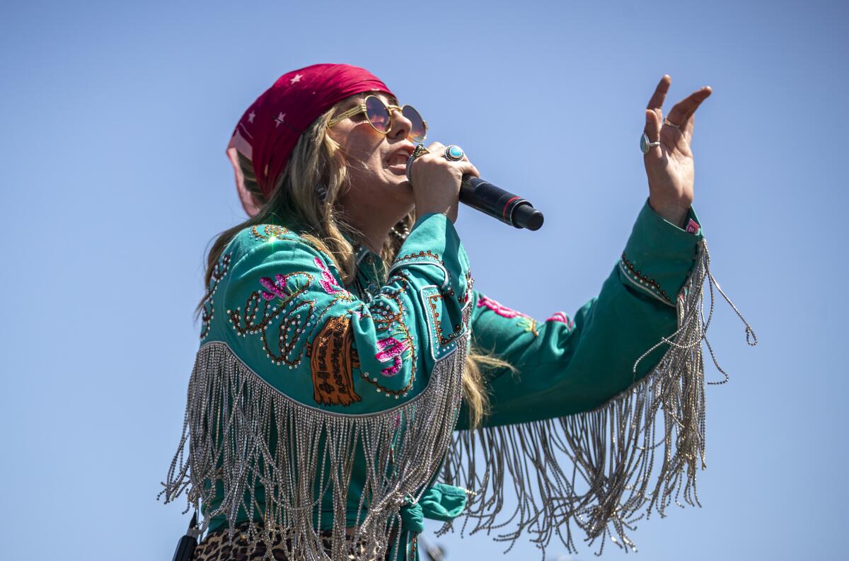 A female country singer in a fringed shirt performs onstage outdoors