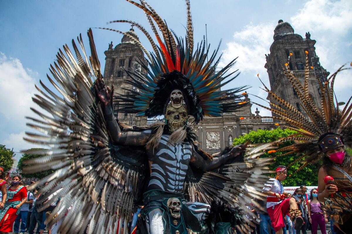 A person in skeleton costume and mask and a headdress adorned with plumes displays feathered wings 