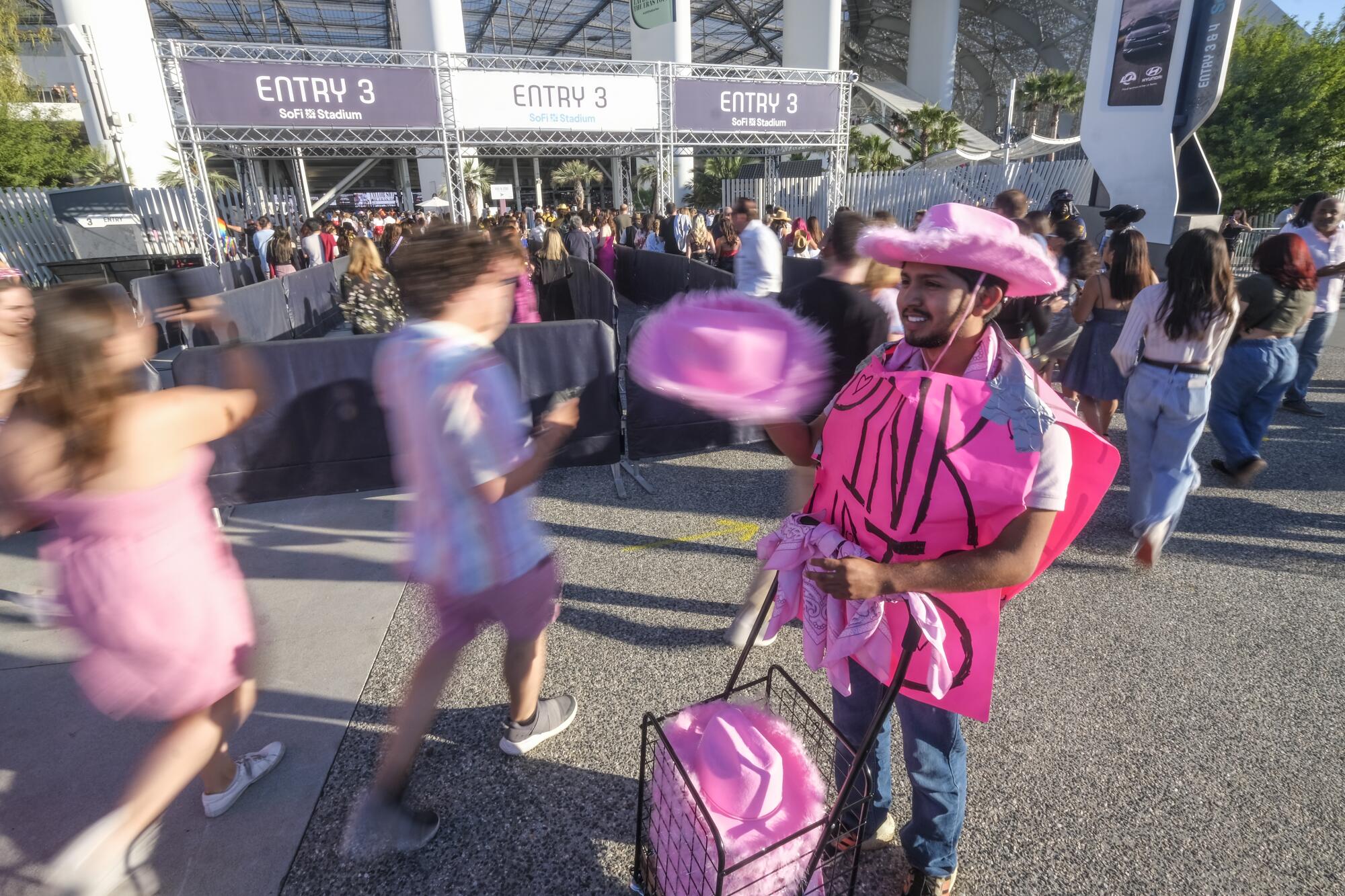 A man hold pink hats while wearing one as people walk past him.