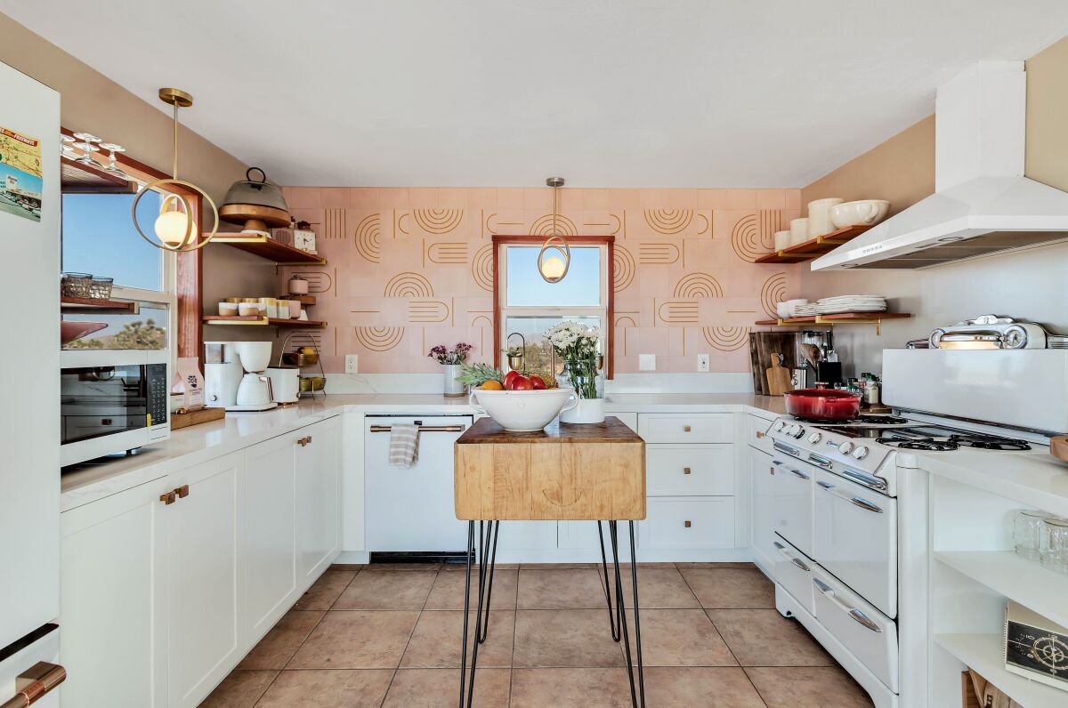 A kicthen with a backsplash of patterned tile and a wooden island on metal legs