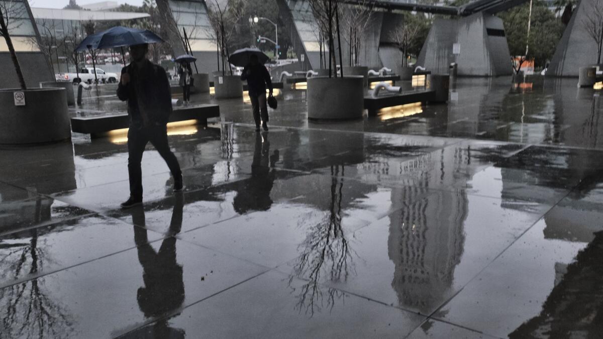 Los Angeles City Hall is reflected in the pavement as office workers arrive at the Caltrans building during the pouring rain in downtown L.A. on Thursday.